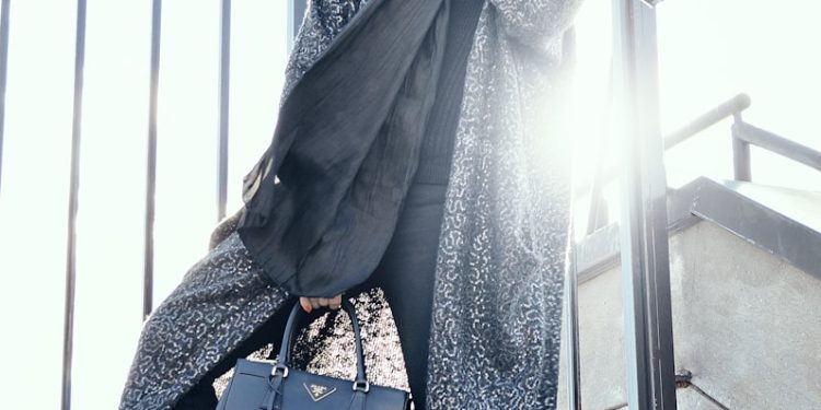 woman in gray coat holding black handbag standing on gray stairs during daytime