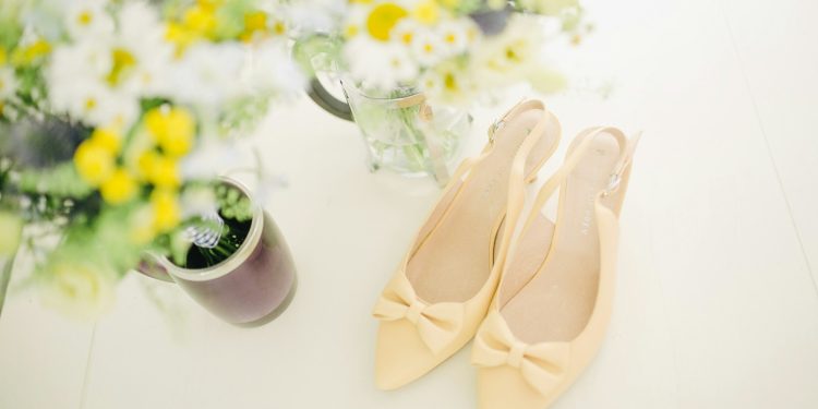 pair of women's beige pointed-toe slingback pumps with ribbons near flower vase